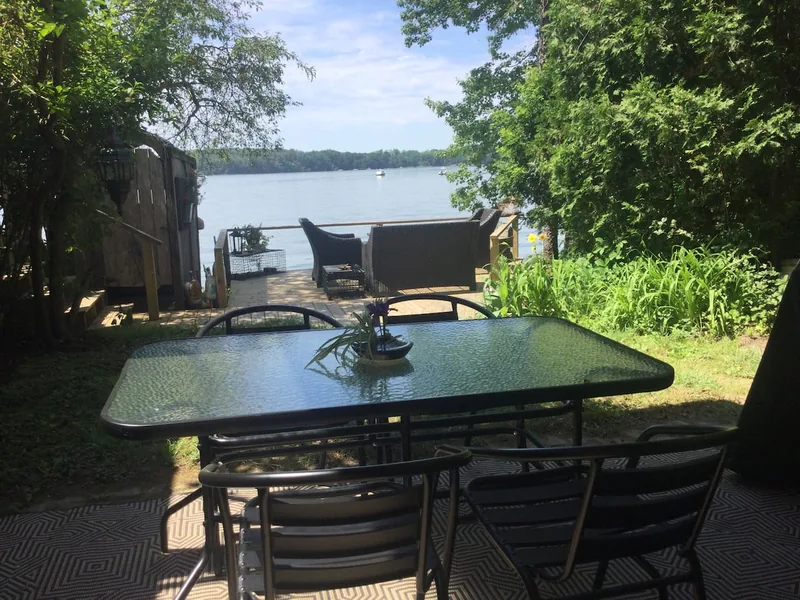 Sunny patio with a glass dining table and chairs overlooking the water and a dock